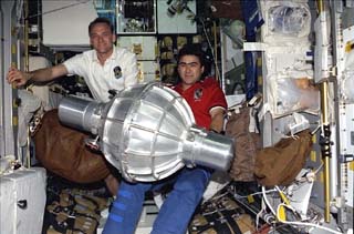 Pilot Joe Edwards and Mission Specialist Salizhan Sharipov hold a gyrodyne onboard the Spacehab intended for transfer to the Mir Space Station.